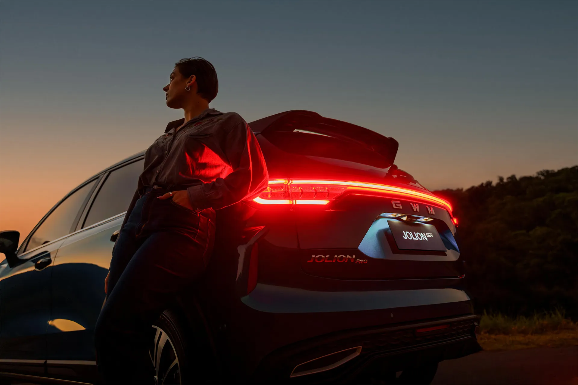 Woman leaning on Haval Jolion Pro at dusk with illuminated tail light